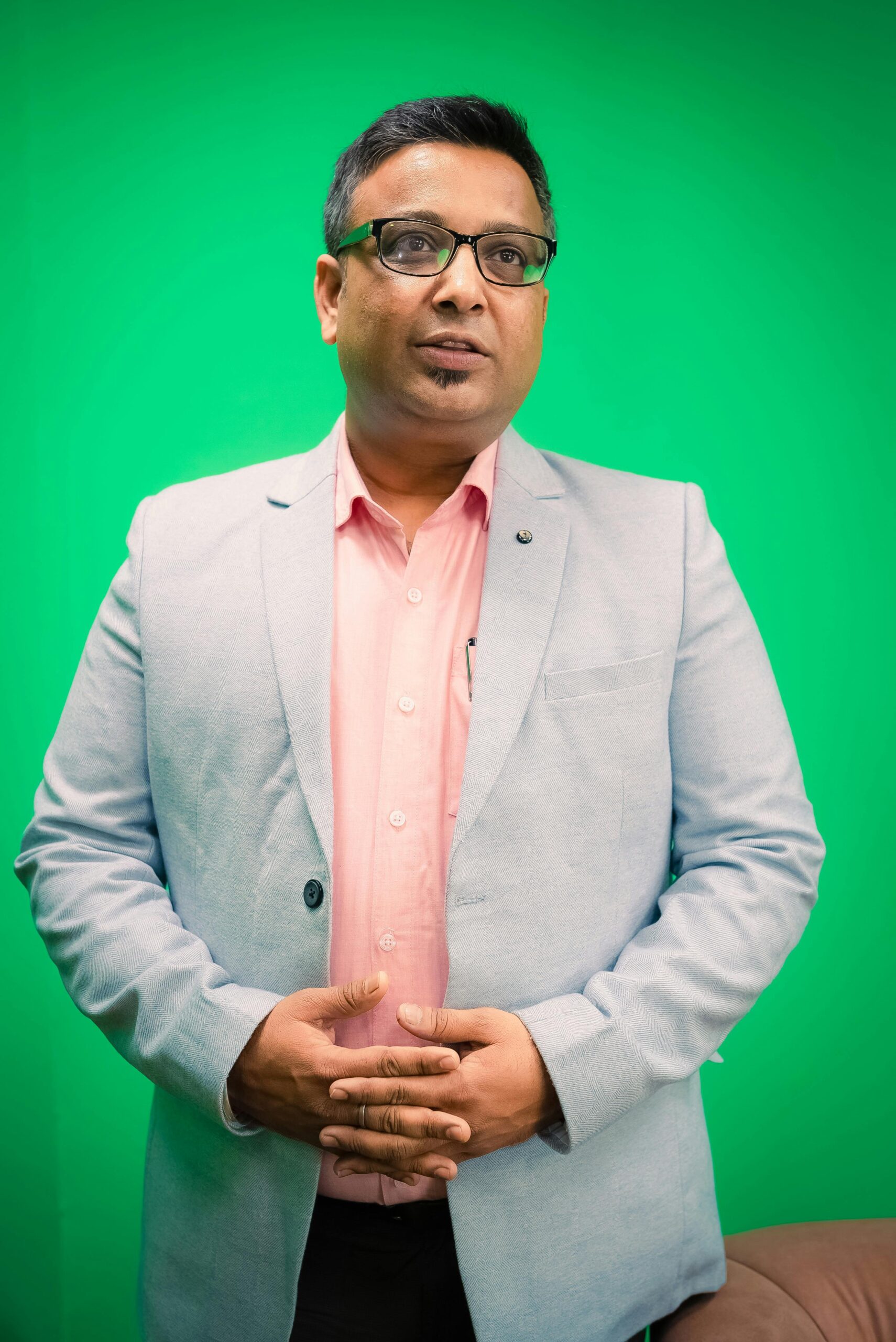Portrait of a South Asian businessman in a light blazer against a green background.
